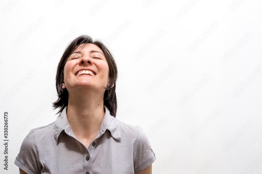 Portrait of a young happy brunette woman standing on a white wall, smiling with closed eyes in a peaceful manner. Positive human emotions. Portrait of a young happy brunette woman standing on a white wall, smiling with closed eyes in a peaceful manner. Positive human emotions.