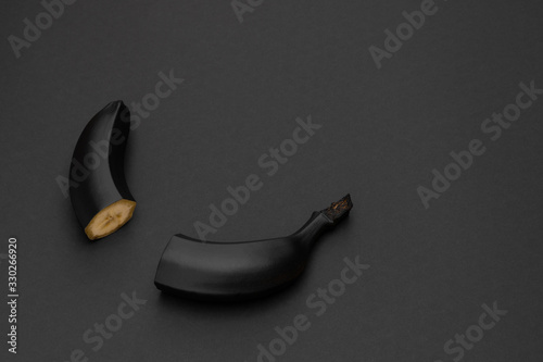 Two halves of a black banana on the matte black background. Minimal style. Conceptual minimalist black art. Matte surface. Cut fruit. One. Space for text