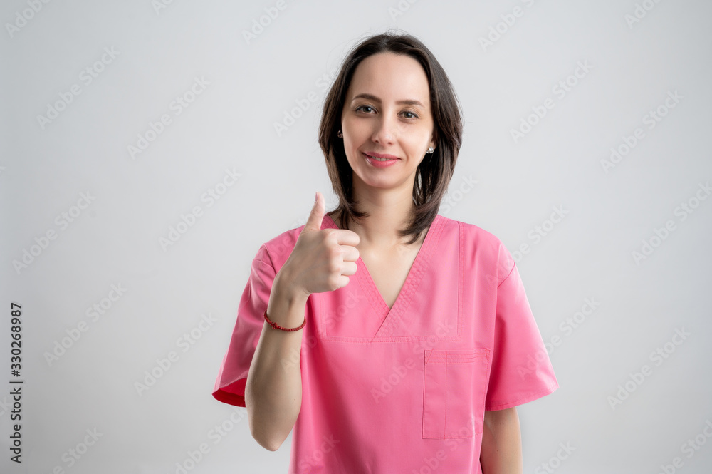 Young woman medical professional nurse or doctor dressed with pink hospital clothes showing thumbs up Young woman medical professional nurse or doctor dressed with pink hospital clothes showing thumbs up