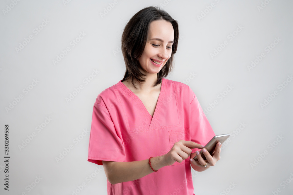 Young woman medical professional nurse or doctor dressed with pink hospital clothes holding smartphone, texting messages happy face Young woman medical professional nurse or doctor dressed with pink hospital clothes holding smartphone, texting messages happy face
