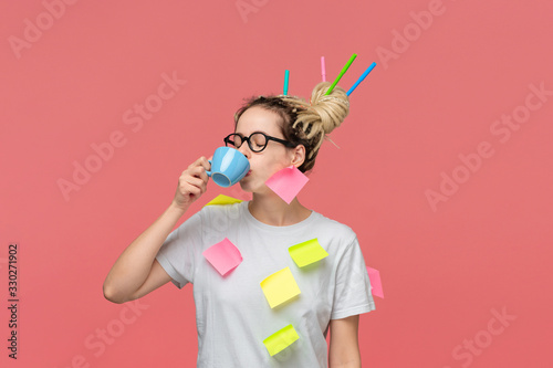 Sleepy student in a white shirt with sticky notes and markers in dreads drinking coffee