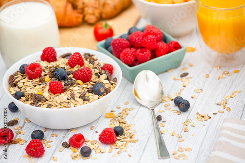 Breakfast Served in the morning with Butter croissant and corn flakes Whole grains and raisins with milk in cups and Strawberry, Blueberry, Raspberry, Kiwi, Fresh Orange Juice on the breakfast table.