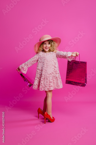 little girl in her mother's big shoes, dress, hat, and shopping bags. baby girl smiling and holding bags from the store. little fashionista on a shopping trip © КРИСТИНА Игумнова