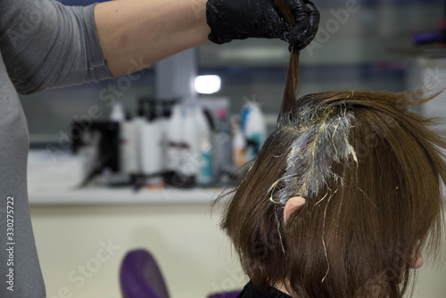 Professional hairdresser putting color mask dyeing hair of woman in beauty salon. Coloring hair spa and care procedures