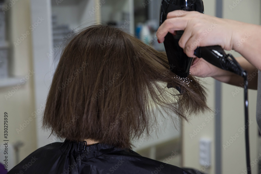 Naklejka premium Professional hairdresser drying woman's hair with hair dryer in beauty salon after beauty procedures and hair coloring