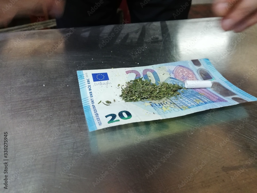 Man preparing and rolling Weed. Marijuana, Cannabis join. hand grinds a  marijuana flower on a twenty euro banknote Stock Photo | Adobe Stock