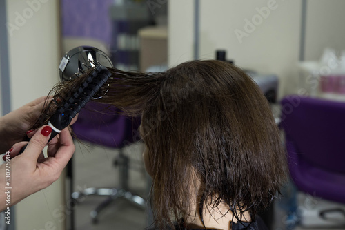 Professional hairdresser drying woman's hair with hair dryer in beauty salon after beauty procedures and hair coloring