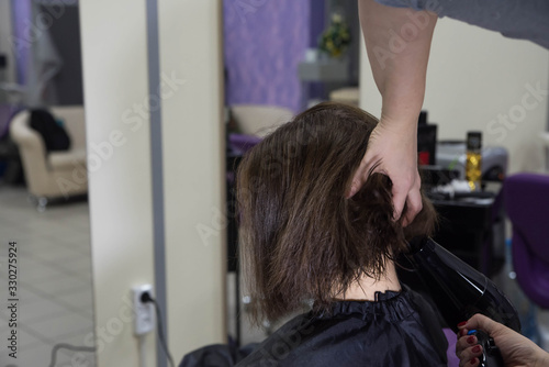 Professional hairdresser drying woman's hair with hair dryer in beauty salon after beauty procedures and hair coloring