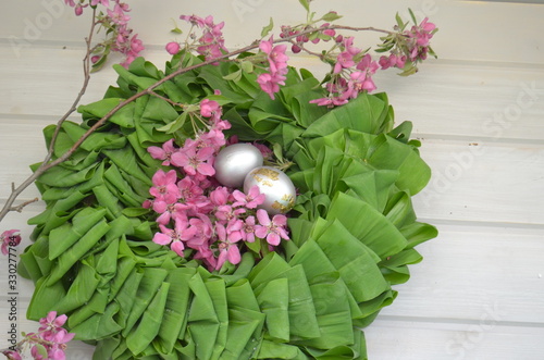 Beautiful festive wreath of green leaves with pink flowers and silver eggs. Easter plants.