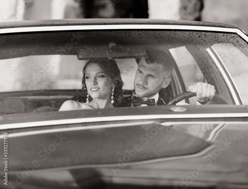 gorgeous bride and handsome groom embracing in vintage car. Wedding couple in retro style.