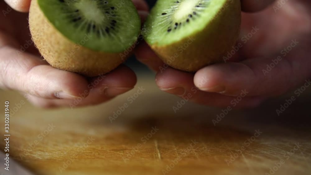 Male hands holding and split opening green kiwi fruit cut in half, SLOW MOTION