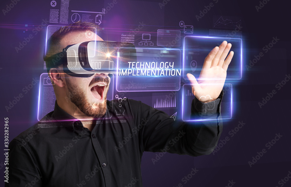 Businessman looking through Virtual Reality glasses with TECHNOLOGY IMPLEMENTATION inscription, new technology concept Businessman looking through Virtual Reality glasses with TECHNOLOGY IMPLEMENTATION inscription, new technology concept