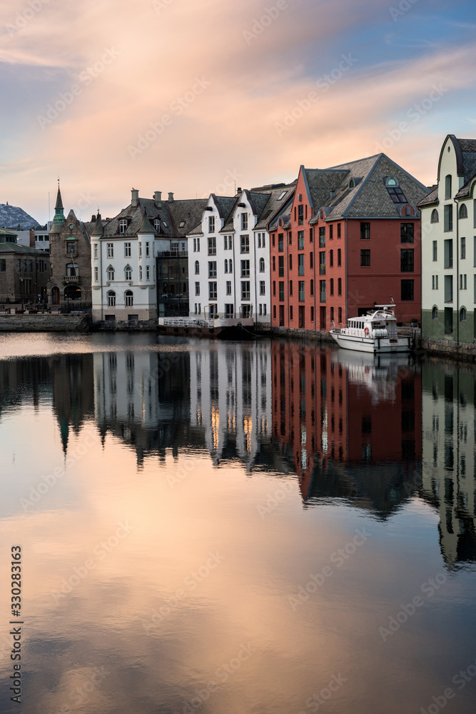 A vertical sunset photograph of beautiful buildings reflecting off the water, taken in Aalesund, Norway.