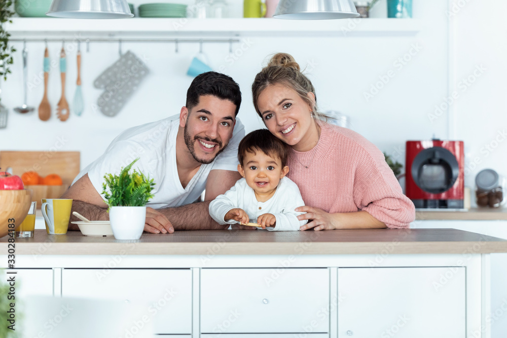 Pretty young parents and they baby son looking at camera in the kitchen at home. Pretty young parents and they baby son looking at camera in the kitchen at home.