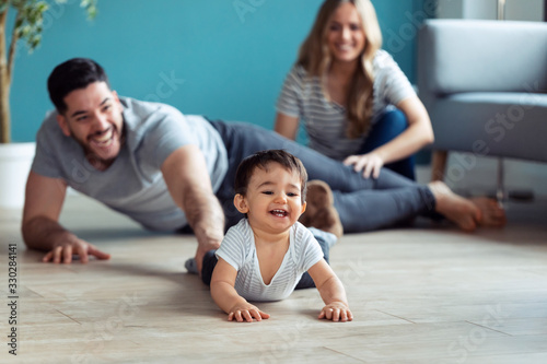 Pretty young parents playing with baby son while sitting on the floor at home.