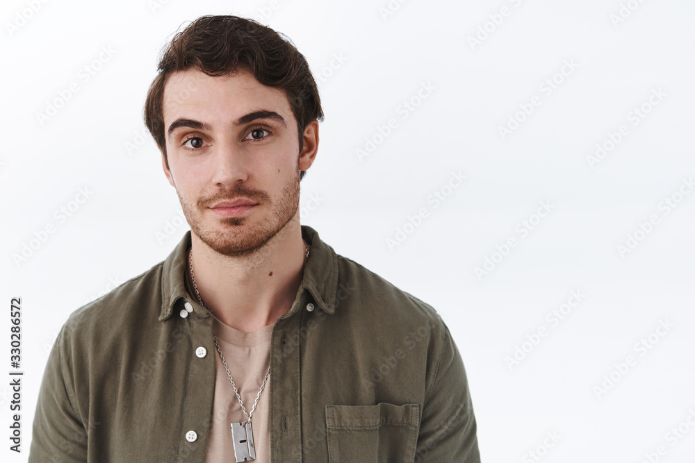 Obraz premium Close-up portrait of handsome macho man with beard in olive shirt, smile cheeky and looking camera with friendly, relaxed expression, standing joyfuly over white background, advertising