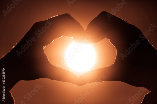 Female hands in heart shape in focus holding sun circle inside