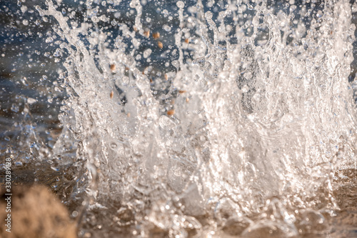 Water spray produced by wave on beachline, selective focus on water splashes