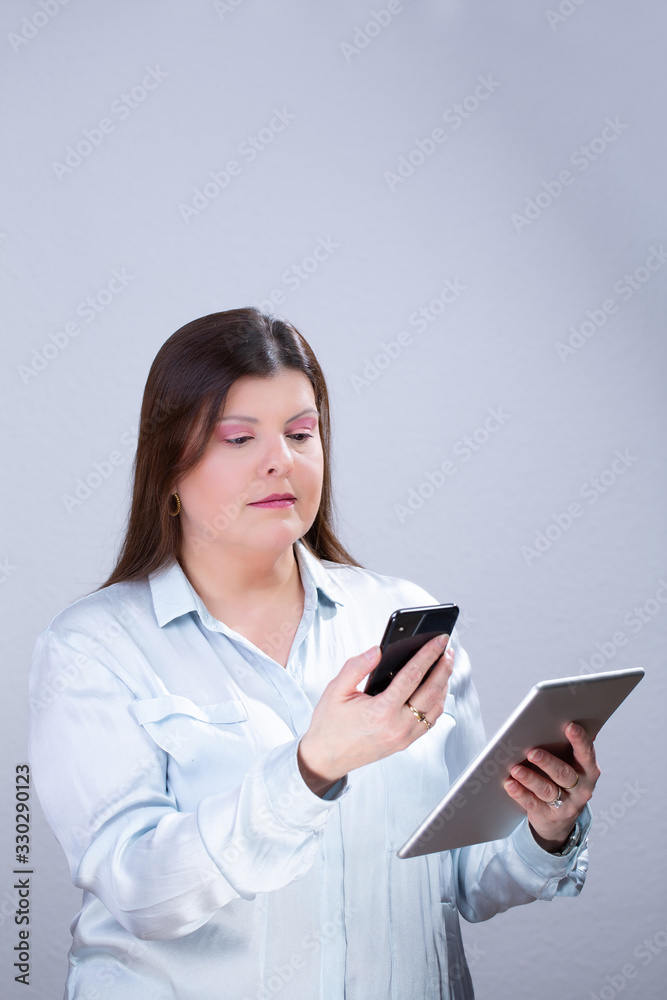 Business Woman Poses for a Studio Portrait. She is texting on her smartphone and reading information from a tablet. Business Woman Poses for a Studio Portrait. She is texting on her smartphone and reading information from a tablet.