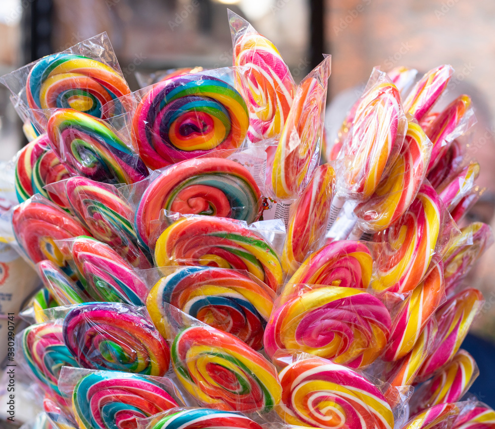 Colorful bright assorted candy canes and rainbow colored spiral lollipops with scattered marmalade, jellybeans and different colored round candy.