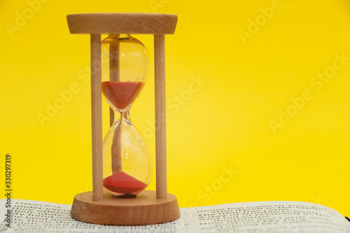 Red sand hourglass on top of open Holy Bible in the Book of the Prophet Ezekiel chapter 7 verse 7. Isolated on yellow background. Close-up. Horizontal shot. photo