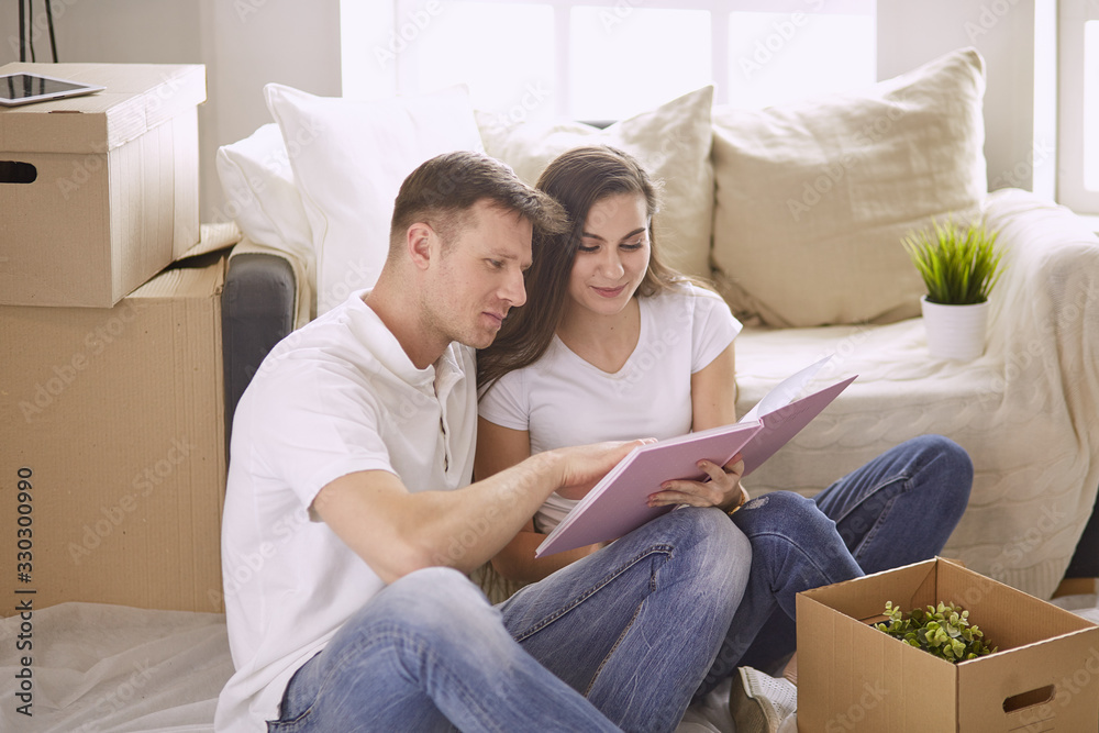 Portrait of happy couple looking at laptop computer together sitting in new house, surrounded with boxes Portrait of happy couple looking at laptop computer together sitting in new house, surrounded with boxes