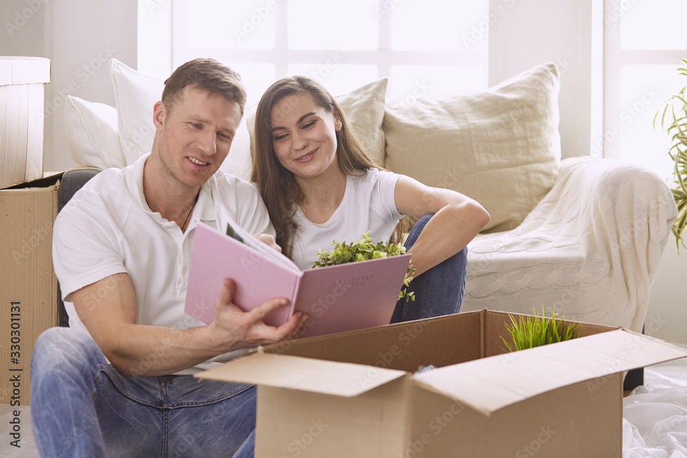 Portrait of happy couple looking at laptop computer together sitting in new house, surrounded with boxes Portrait of happy couple looking at laptop computer together sitting in new house, surrounded with boxes