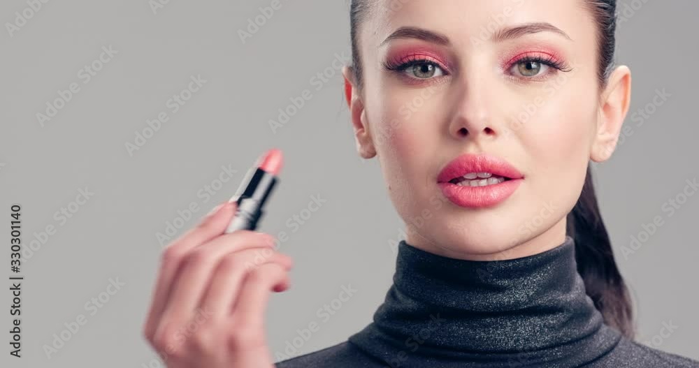 Young woman paints her lips with lipstick. Beautiful brunette model doing make-up. Woman makes makeup before camera.  Cosmetic concept. 4k Slow motion footage. Closeup view.