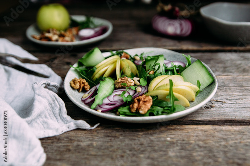 Vegetarian salad of fresh apples with arugula, onions and nuts in a plate on the table