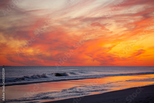 Vibrant pink and orange sunset over small waves breaking on the beach. Jones Beach, Long Island New York