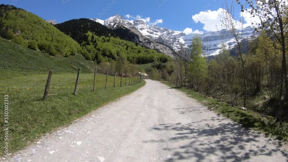 Hiking in Valley of the Pyrenees Mountains looking up Towards the Snow Capped Mountain Peaks with Green Mountain Pastures Lining the Hiking Path in Southern France on a Blue Sky Spring Day Hiking in Valley of the Pyrenees Mountains looking up Towards the Snow Capped Mountain Peaks with Green Mountain Pastures Lining the Hiking Path in Southern France on a Blue Sky Spring Day