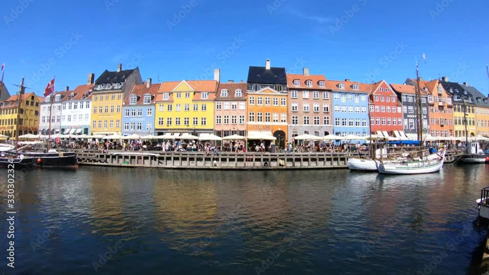 Tourists Walking around Nyhavn Harbor With Views of Sailboats and Colorful Buildings Reflecting in the Water on a Clear Sunny Day Tourists Walking around Nyhavn Harbor With Views of Sailboats and Colorful Buildings Reflecting in the Water on a Clear Sunny Day