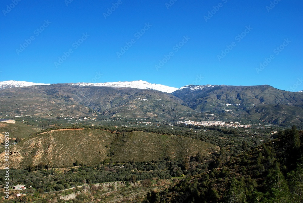Fototapeta premium View of the town and countryside in the Vale of Lecrin with views towards the snow capped Sierra Nevada mountains, Orgiva, Spain.