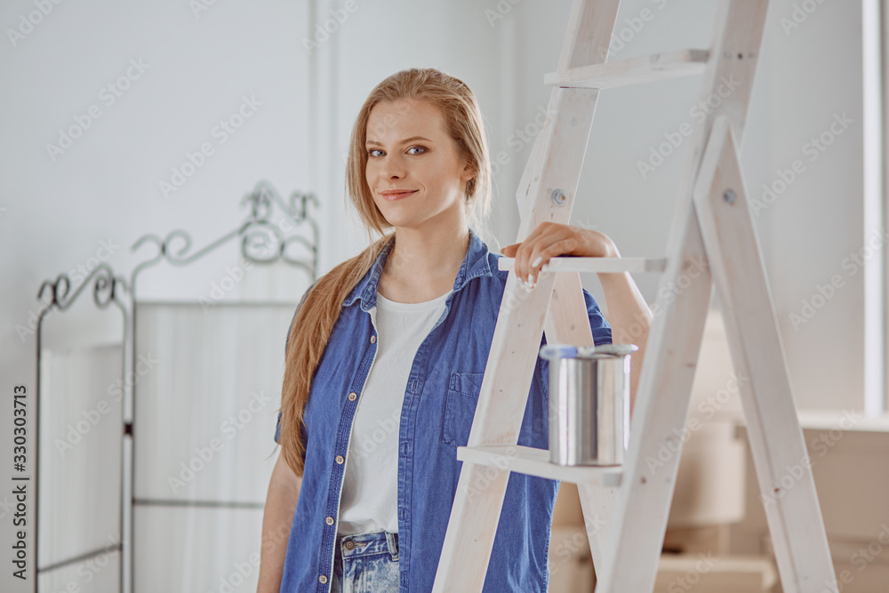 Beautiful young woman on a white wooden stepladder. Ready to repair the room. Women housework concept Beautiful young woman on a white wooden stepladder. Ready to repair the room. Women housework concept