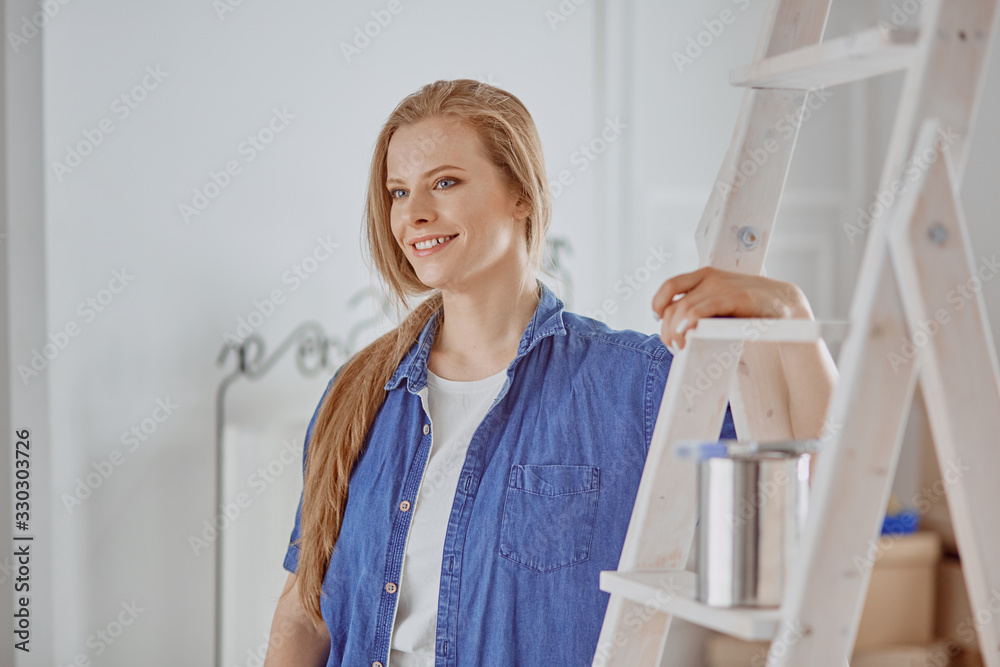 Beautiful young woman on a white wooden stepladder. Ready to repair the room. Women housework concept Beautiful young woman on a white wooden stepladder. Ready to repair the room. Women housework concept