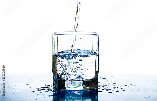 A stream of water pours into a glass on a white background. Water drops on the table.