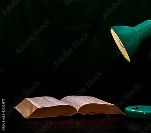 An open old book and a table lamp on a black background.