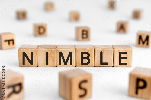 Nimble - word from wooden blocks with letters, quick agile nimble concept, random letters around white background