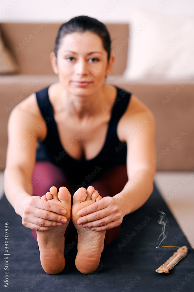 Fototapeta premium Young sporty woman practicing yoga, doing Seated forward bend, head to knee exercise, paschimottanasana pose, working out, indoor close up, at yoga studio