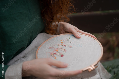 Принти на полотні Hands of girl / woman / female in boho linen dress hold sewing stitching pattern in embroidery frame on the background of park