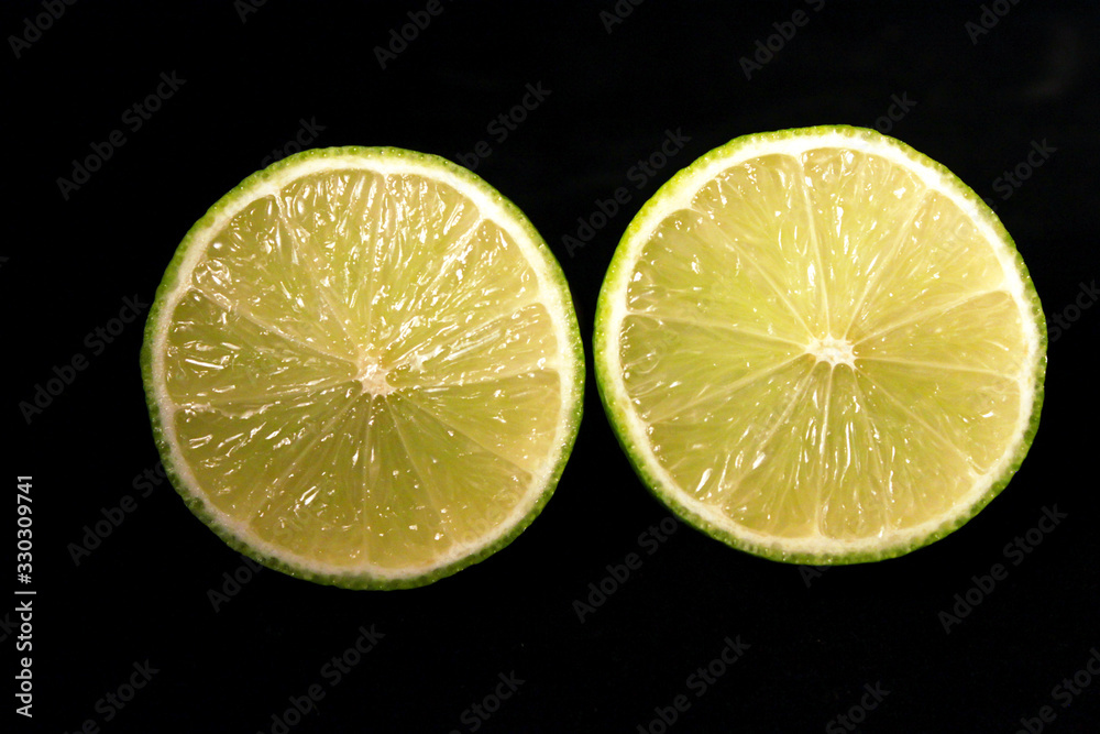 Lime slices isolated on black background. Two green fresh limes cut in half close-up. Design element Lime slices isolated on black background. Two green fresh limes cut in half close-up. Design element
