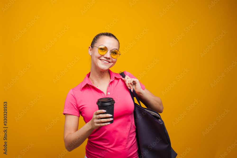 Cute blonde in sunglasses and t-shirt with bag on shoulder, drinking her hot drink, portrait on yellow background Cute blonde in sunglasses and t-shirt with bag on shoulder, drinking her hot drink, portrait on yellow background