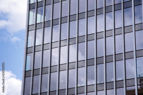 Modern curtain wall made of glass and steel. Blue sky and clouds reflected in windows of modern office building. 