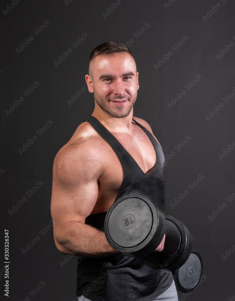 Bodybuilder with dumbbells on black background stands and shakes her bicep.