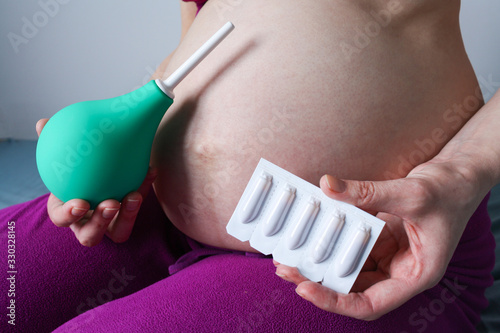 A pregnant girl holds an enema and rectal candles in front of her. suppository. photo