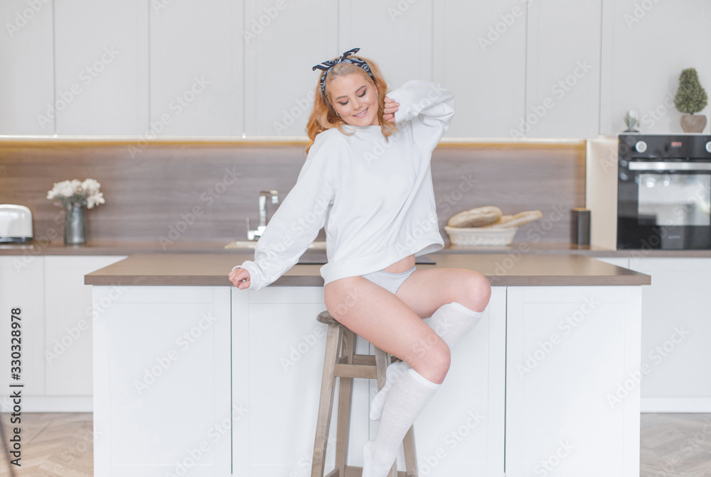Happy young girl in white sweatshirt and white stockings and panties posing on chair in kitchen Happy young girl in white sweatshirt and white stockings and panties posing on chair in kitchen