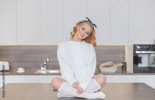 Quadro su tela Sexy  blonde in white sweatshirt and knee socks sits with crossed legs on the ki