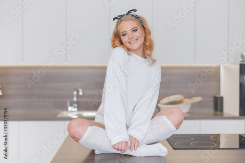Foto Sexy smiling blonde in white sweatshirt and knee socks sitting in Turkish pose o