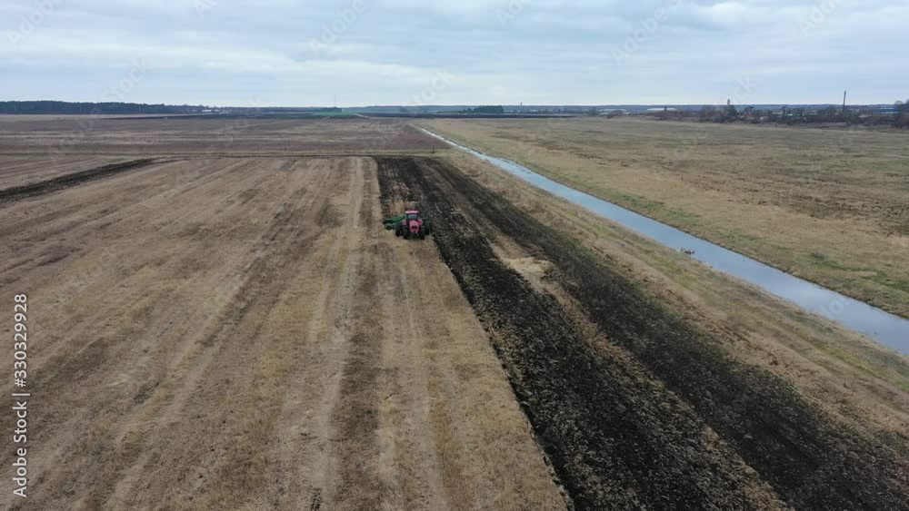 Cloudy day after rain. Farm machinery on the field. Agricultural landscape from the air. Tractor on a plowed field. Agricultural field for planting vegetables. Tractor makes furrows on the field