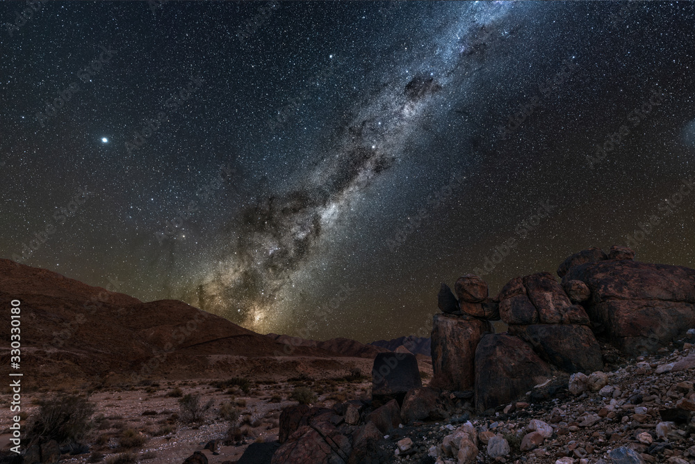 A beautiful night sky landscape with the Milky Way and galactic centre, and interesting rock formations in the foreground and mountains on the horizon, in the Richtersveld National Park, South Africa.